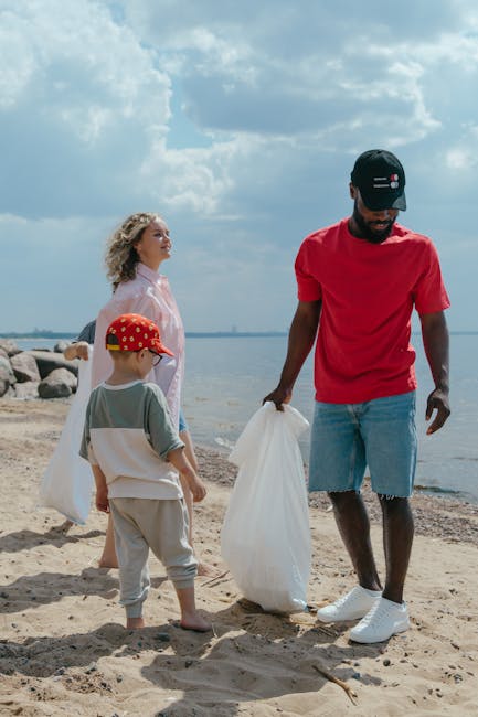 A person wearing a light blue t-shirt, black shorts, and white sneakers with green accents is standing on a rocky shoreline near a body of water. They are holding a litter picker in their right hand and have a plastic rubbish bag in their left hand, suggesting they are engaged in collecting debris or rubbish from the area. The rocks are of various sizes, predominantly dark grey and brown, with some patches of green moss or algae visible on the surface, indicating a damp environment. The background shows the water’s surface, which is calm with gentle ripples, and the scene is illuminated with natural daylight, creating a clear and neutral atmosphere. The individual’s posture and the presence of litter collection tools imply that they are participating in an outdoor rubbish removal activity, aligning with private waste disposal efforts outside of municipal services, typical of independent rubbish removal practices in coastal or shoreline environments. Rubbish Removal Bayswater offers services related to rubbish clearance, which can include on-site collection in similarly natural or urban settings.